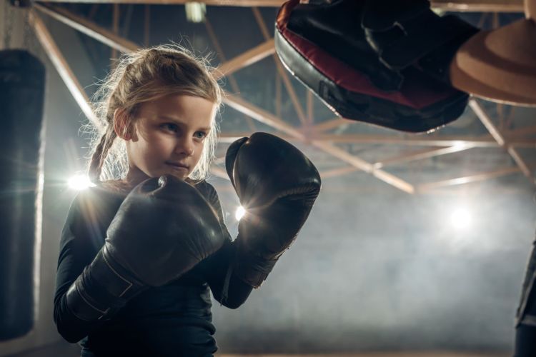 Small girl exercising boxing with unrecognizable coach in a health club.
