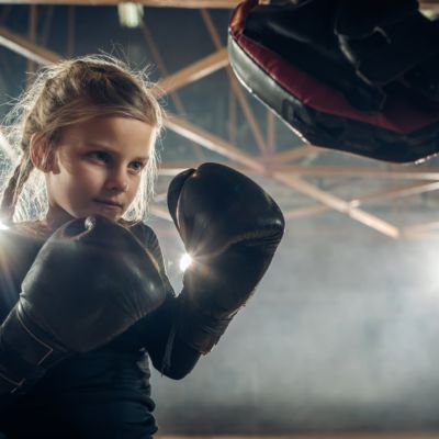 Small girl exercising boxing with unrecognizable coach in a health club.